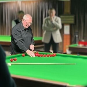 Dennis Taylor setting up for a trick shot. He has lined up red balls in an arch near the corner pocket. He intends to jump the ball over the top into the pocket.