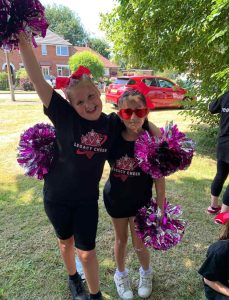 Two girls from Legacy Cheer waving pink and purple pom poms.