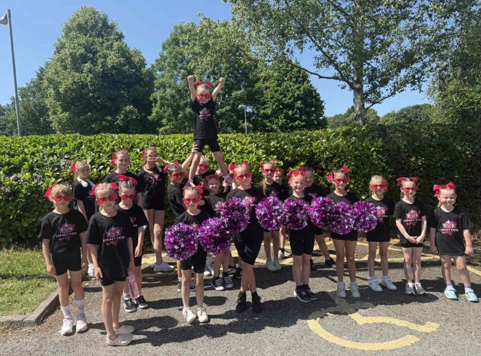 Legacy Cheer teams members wearing thier black uniform with purple pom poms. Members are aged between 5 and 10.
