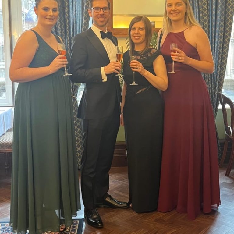 Melissa Howman, Paul Clark, Becky Spall and Natasha Yelland in evenving wear at the St James Club, Standing in front of a window with champagne.