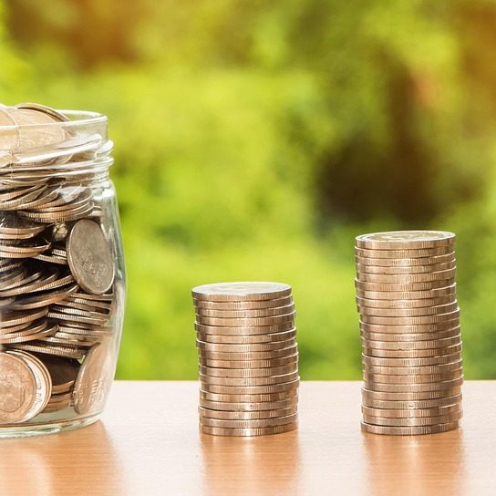 Coins in a jar with three small stacks of coins next to the jar. Each stack is slightly larger than the previous.