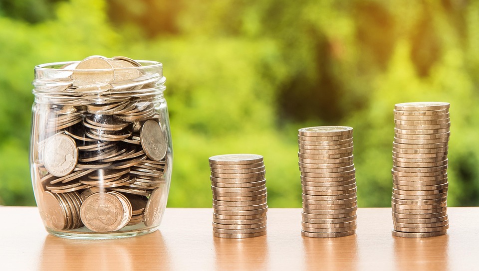 Money Coins in a jar with three small stacks of coins next to the jar. Each stack is slightly larger than the previous.